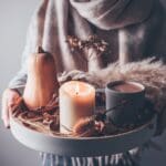 person holding beige pillar candle on gray wooden tray